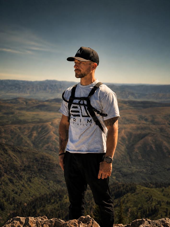 Man wearing The Vanguard black curved-brim snapback on a mountain summit overlooking a forested valley