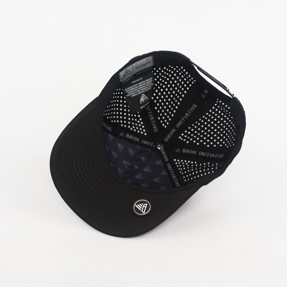 Underside of The Vanguard snapback showing the patterned under-brim, laser-cut crown venting, BRIM Initiative taped seams and a round PVC logo patch